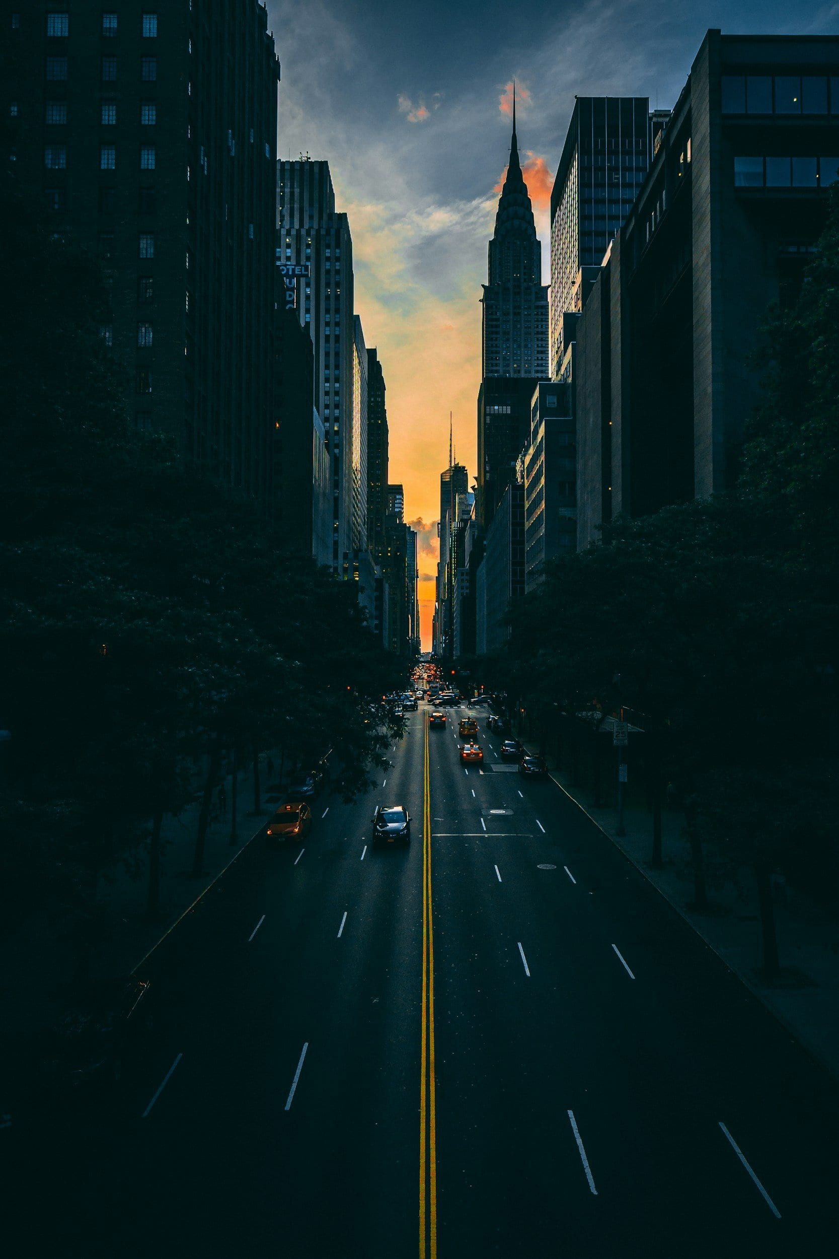 City street during sunset, tall buildings on each side and the Chrysler Building in the distance.